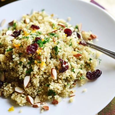 Golden quinoa and herb pilaf with citrus finished with toasted almonds and cranberries, ready for a Mediterranean dinner plate.