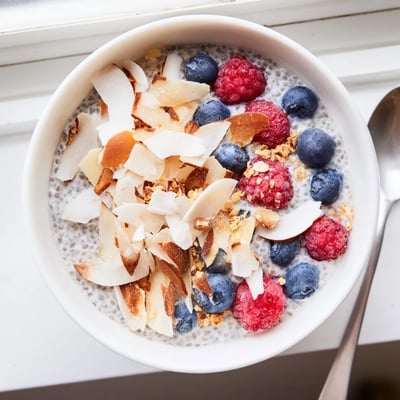 Creamy Coconut Almond Chia Pudding served chilled in a glass with shredded coconut and raspberries.  