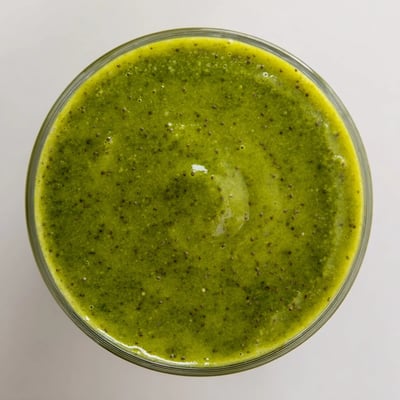 The Kale Pineapple Spinach Smoothie is blended to creamy perfection in a blender, with fresh kale and pineapple chunks visible beside the finished drink.