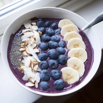 Thick Blueberry Banana Almond Smoothie Bowl crowned with sliced banana, almonds, and toasted coconut